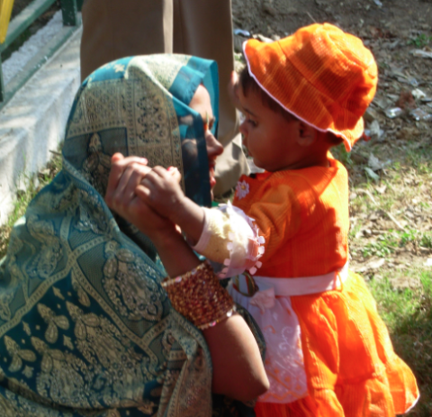 Woman in blue headscarf talking to child in orange dress