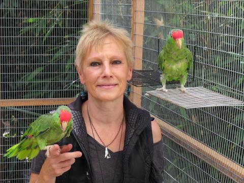 Ursula Heise smilimg with one parrot perched on her right, another on her left hand