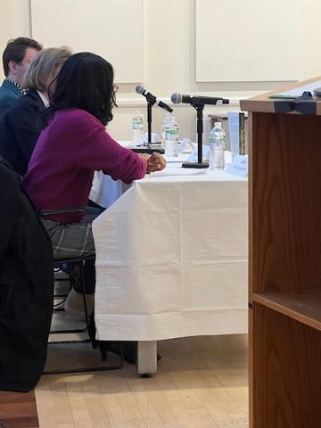 three people in profile at a table with microphones