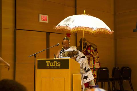 Ghanian chief in traditional clothing, speaking at microphone with umbrella