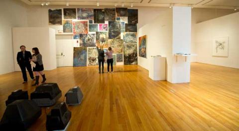 museum room with collage of paintings on back wall