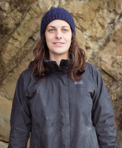Fern Thompsett in a jacket and knit hat near a rock wall