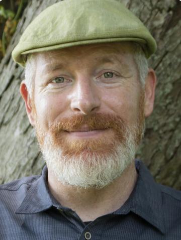 Mark bomford's face, standing in front of a tree