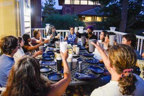 Students sitting outside around a table raising a glass in celebration