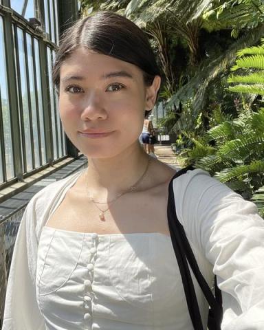 Rachel Tang in a white shirt, with plants and a window behind her