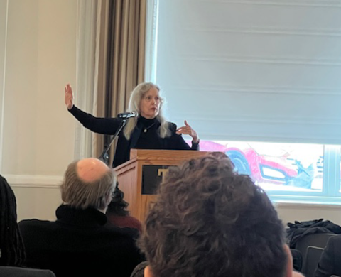 Elaine Scarry standing in front of a microphone and podium