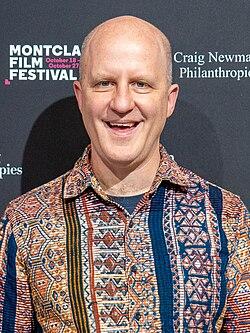 Sandi DuBowski standing in front of a dark background in a patterned shirt