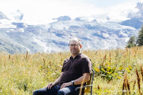 Rob Wallace sitting in a field with mountains in the distance