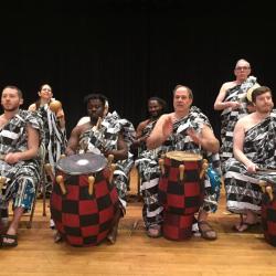 men on stage in traditional asante dress, using drumps