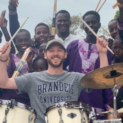 Ben paulding playing drums with smiling people in purple behind him