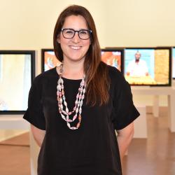 Erica Jones standing near some Tv monitors, wearing a black dress