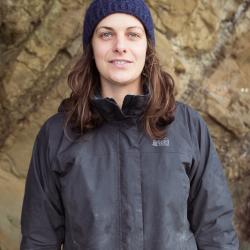 Fern Thompsett in a jacket and knit hat near a rock wall