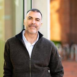 Rich Jankowsky on a sidewalk, in a black jacket, leaning on a glass wall