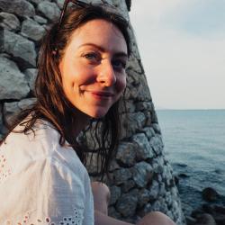 Amy Claire standing at the seaside with a rock wall on her left