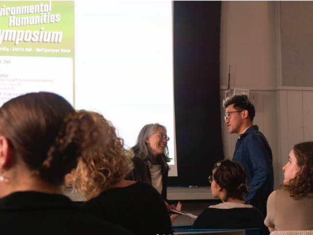 two people talking, and others in chairs, facing a projection screen