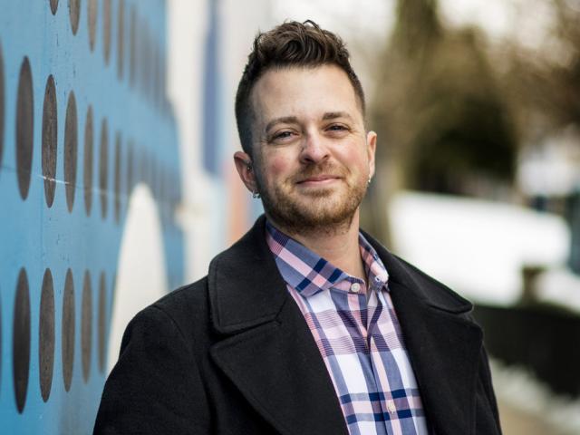 profile headshot of KJ Rawson standing outdoors near a blue wall