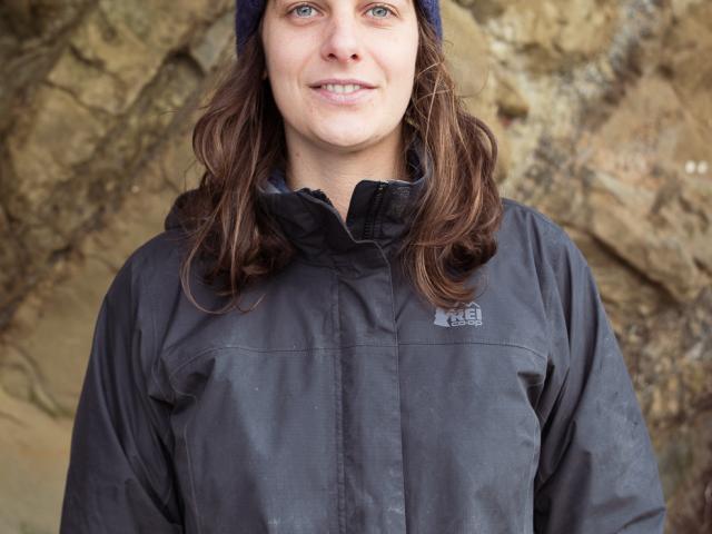Fern Thompsett in a jacket and knit hat near a rock wall