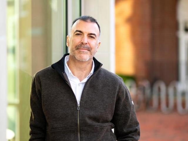 Rich Jankowsky on a sidewalk, in a black jacket, leaning on a glass wall