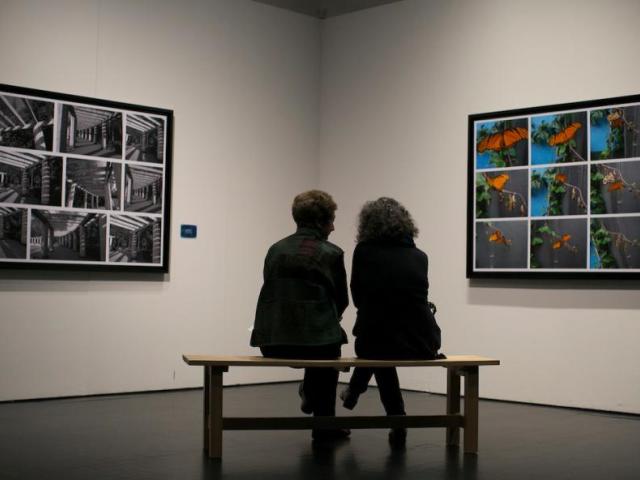 two people sitting on a bench, looking at art on a wall