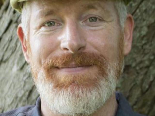 Mark bomford's face, standing in front of a tree