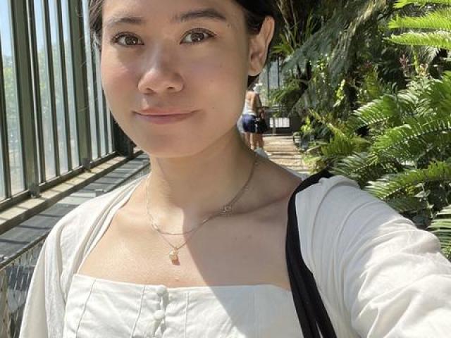 Rachel Tang in a white shirt, with plants and a window behind her