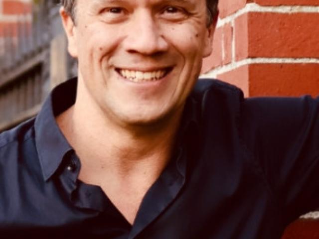Lin Fisher standing next to a brick wall, wearing a black shirt